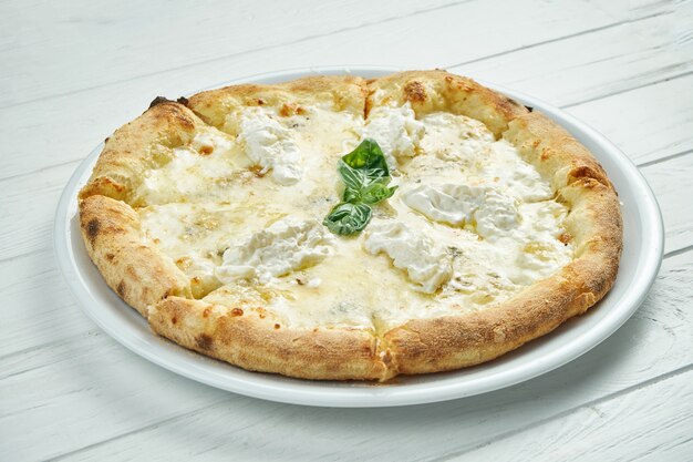 Appetitosa pizza fatta in casa a 4 formaggi con gorgonzola, mozzarella, parmigiano e strachatella su un piatto bianco su un bianco