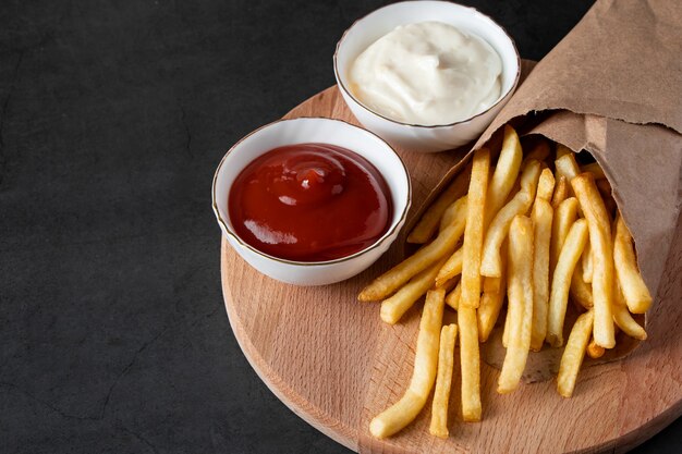 Appetitose patatine fritte croccanti in un sacchetto di carta ecologico su sfondo nero. Fast food americano caldo.