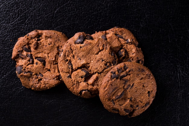 Appetitosi biscotti al cioccolato con fette di uva passa su un muro nero.