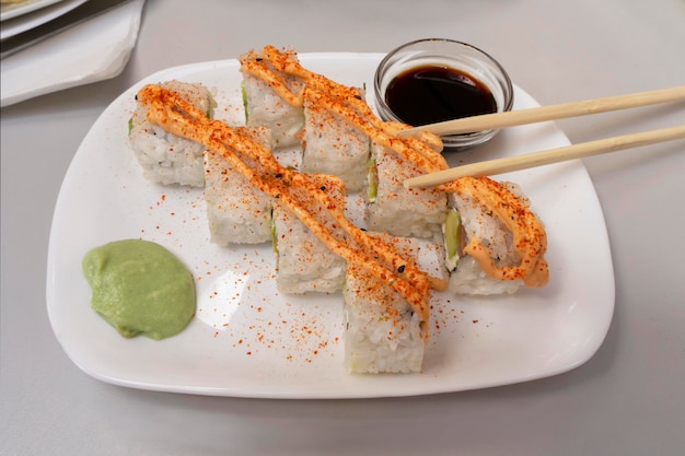 Appetitosi involtini di riso sushi con avocado e pesce rosso guarniti con maionese speziata su un piatto con salsa di soia wasabi e bastoncini di legno giapponesi Sushi tradizionale giapponese su un piatto in una res