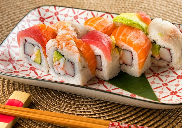 Appetitosi involtini di sushi uramaki arcobaleno con granchio e avocado conditi con tipi assortiti di pesce serviti su un piatto vicino alle bacchette in un ristorante moderno