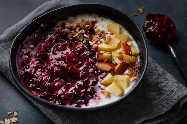 Appetitoso muesli fatto in casa con frutti di bosco e yogurt servito in una ciotola su sfondo scuro.