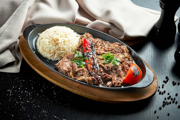 Appetitoso piatto turco - agnello al forno, con verdure grigliate e riso in una padella nera su un tavolo nero