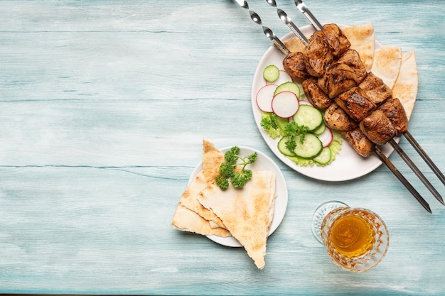 Appetitoso shish kebab fatto in casa, verdure a fette, un bicchiere di vino vista dall'alto su uno sfondo di legno blu.