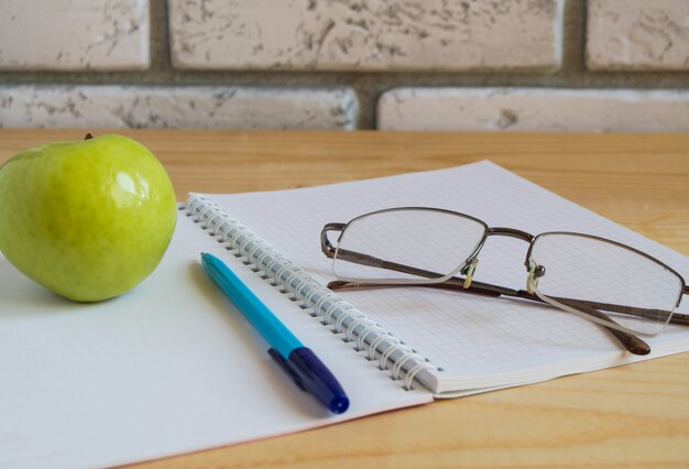 Apple, notebook, occhiali da lettura e penna sul tavolo di legno.