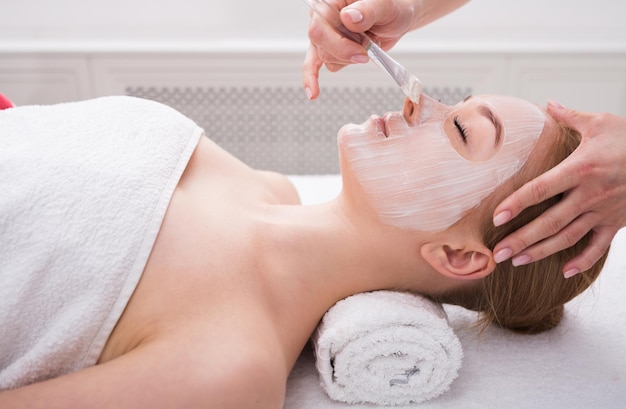 Applicare maschera per il viso, trattamento di bellezza spa e cura della pelle. Donna che ottiene maschera nutriente facciale dall'estetista al salone della stazione termale, primo piano