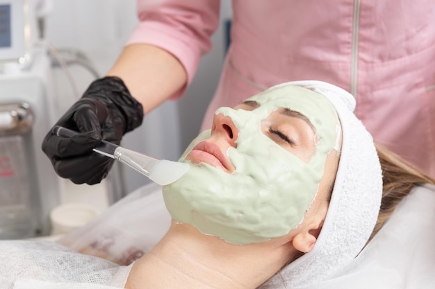 Applicazione di una maschera facciale verde chiaro con pennello nella medicina alternativa per il trattamento termale.