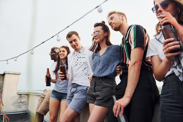 Appoggiato sul bordo del tetto con decorazioni Gruppo di giovani in abiti casual organizzano una festa insieme durante il giorno