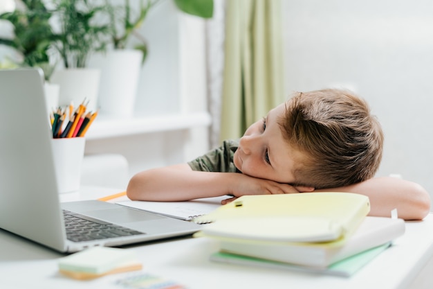 Apprendimento a distanza educazione online bambino caucasico studia a casa al laptop sonno stanco e pisolino