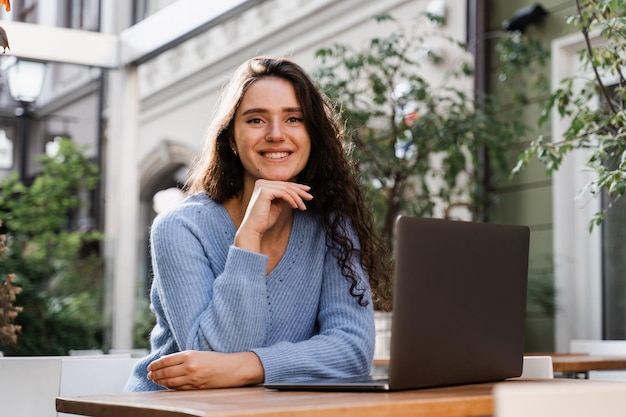 Apprendimento a distanza Ragazza attraente che digita e chatta sul laptop all'aperto in un caffè Insegnante di inglese concentrato con laptop ha lezioni online tramite comunicazione video all'esterno