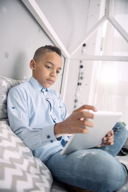 Apprendimento della vita. Ragazzo afroamericano concentrato bello facendo uso della compressa mentre fissava