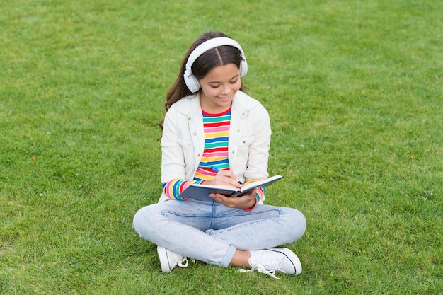 Apprendimento online Podcast educativo Make It Happen Ascolta musica all'aperto Cuffie per ragazza cool che ascolta musica Kid girl goditi la musica siediti sul prato Tempo piacevole Cuffie per bambini ascolta musica