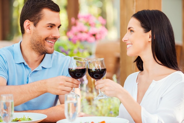 Appuntamento romantico al ristorante. Felice giovane coppia di innamorati che brindano con vino rosso e sorridono mentre si rilassano insieme nel ristorante all'aperto