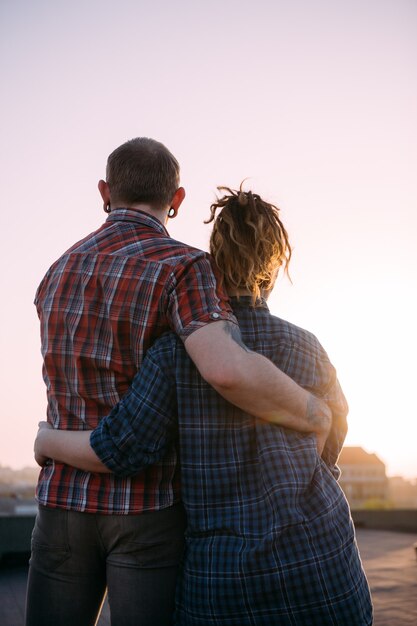 Appuntamento romantico all'aperto. Coppia d'amore coccole. Persone irriconoscibili insieme che si godono il tramonto sul tetto, eleganti hipster moderni in primo piano, sfondo urbano con spazio libero free