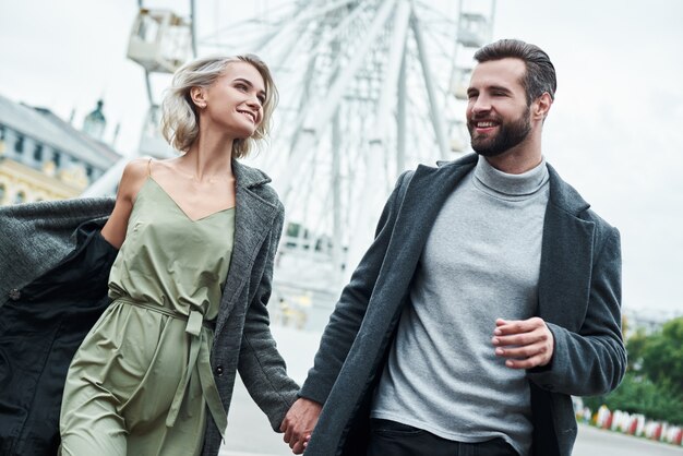 Appuntamento romantico all'aperto giovane coppia che corre al parco divertimenti tenendosi per mano guardandosi ciascuno