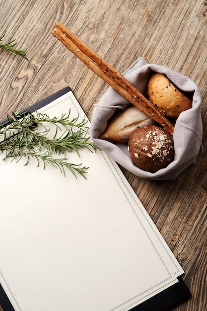 Appunti del menu del ristorante di Natale con lo spazio della copia per testo. Appunti di carta in bianco con ramo di albero di Natale e pane sul fondo della tavola in legno