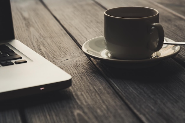 Apra il computer portatile e una tazza di caffè su un primo piano di legno nero della piattaforma