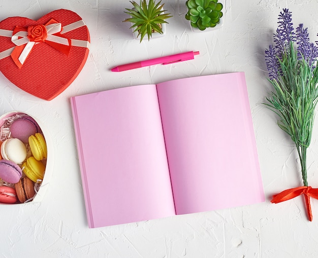 Apra il taccuino con le pagine rosa in bianco, la matita rossa e verde e un mazzo di lavanda sulla vista bianca e superiore