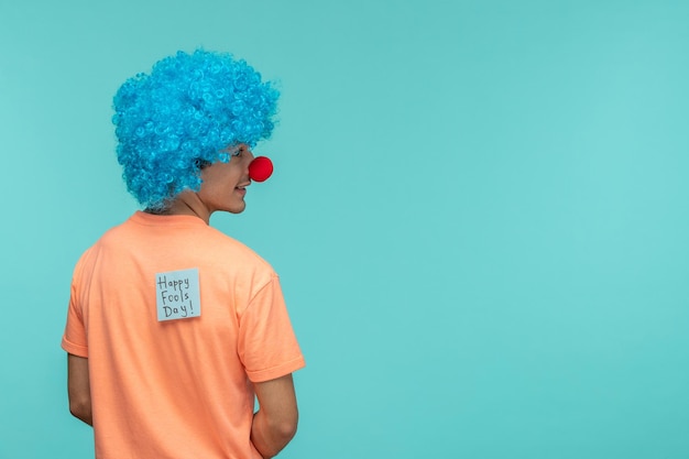 April Fools Day ragazzo pagliaccio sorridente guardando al lato capelli blu blu postit adesivo nota divertente naso rosso