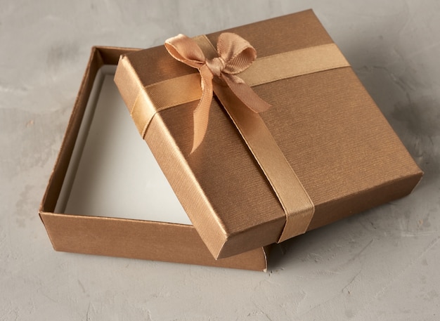 Aprire il contenitore di regalo quadrato dorato su sfondo grigio