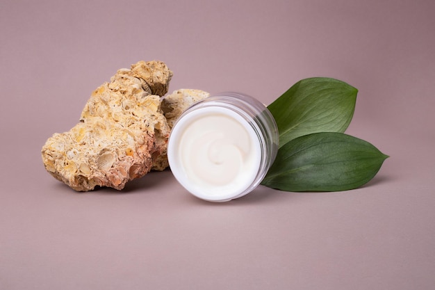 Aprire il contenitore per cosmetici con crema bianca e foglie verdi lucide su sfondoconcetto ecologico