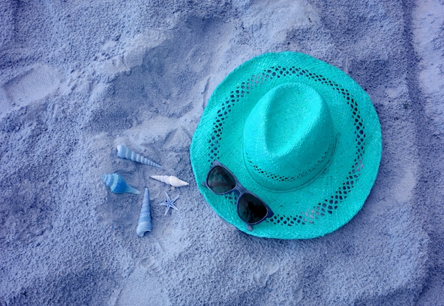 Aqua blu colorato di cappello di paglia con occhiali da sole e molte conchiglie sulla spiaggia di sabbia