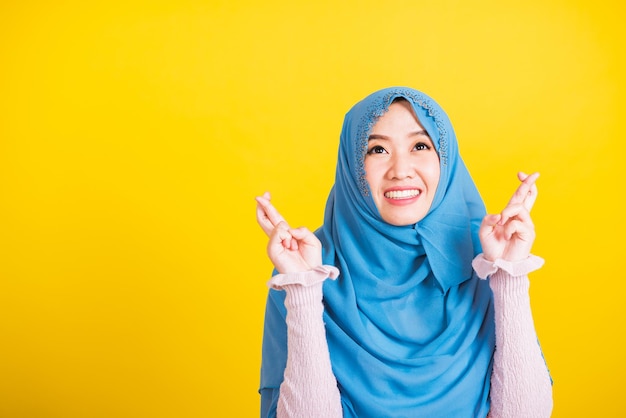 Arabo musulmano asiatico, Ritratto di felice asiatica bella giovane donna religiosa islamica indossare velo hijab lei sorride e tiene le dita incrociate per buona fortuna, girato in studio isolato su sfondo giallo