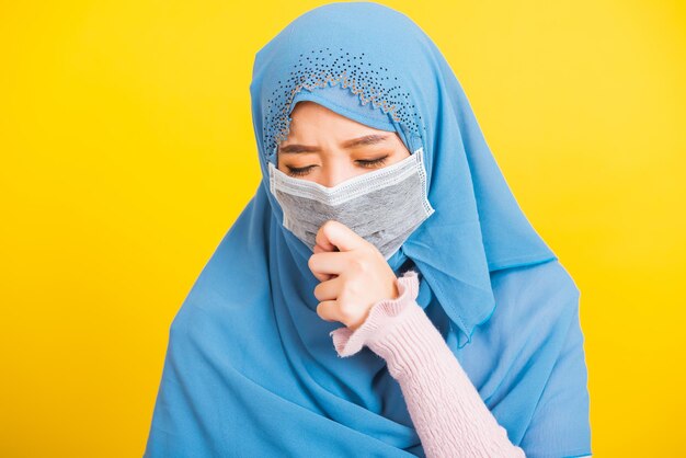 Arabo musulmano asiatico, Ritratto di felice bella giovane donna religiosa indossa velo hijab indossa una maschera protettiva, epidemia di coronavirus usa la bocca chiusa e starnutisce, isolato sfondo giallo