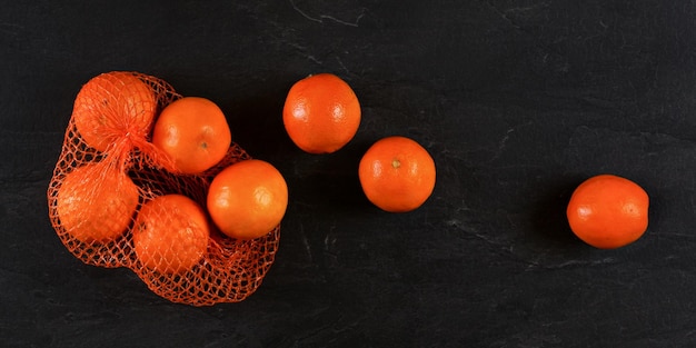 Arance in rete di plastica rossa da supermercato, alcune sparse su pietra nera come una tavola, foto dall'alto