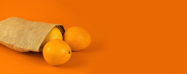 Arance in un sacchetto di iuta naturale su uno sfondo arancione. Layout con copia spazio.