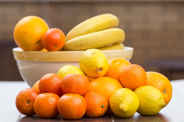 Arance, limoni e mandarini in un mucchio e dietro un cesto di frutta con agrumi e banane