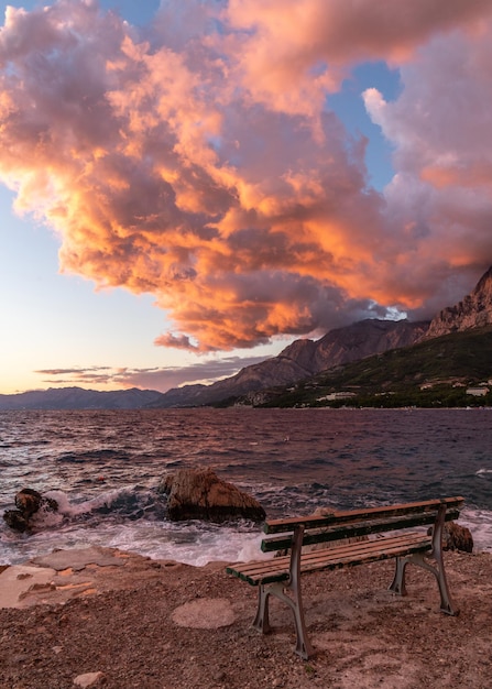 Arancione tramonto sul mare C'è una panchina sulla riva Paesaggio montano Rosso arancione nuvole e s