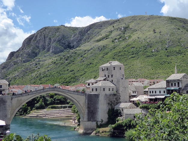 Arch bridge over river by buildings and mountains against sky