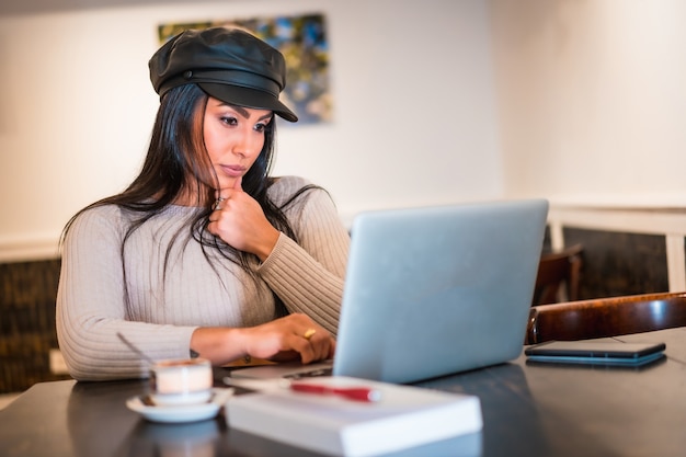 Architetto bruna latina che legge e-mail di lavoro con il telelavoro al computer da una caffetteria