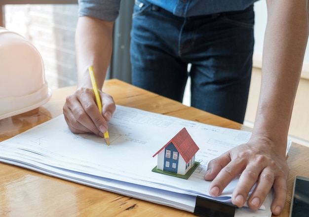 Architetto che tiene una pianta della casa del disegno a matita gialla con la casa di modello sulla pianta.