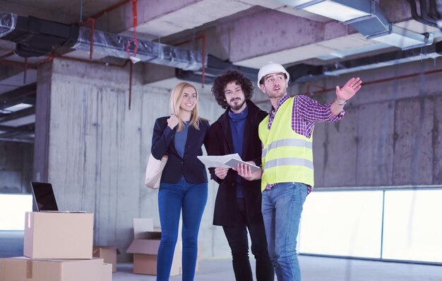 architetto che utilizza un computer tablet mentre mostra i piani di progettazione della casa a una giovane coppia in cantiere