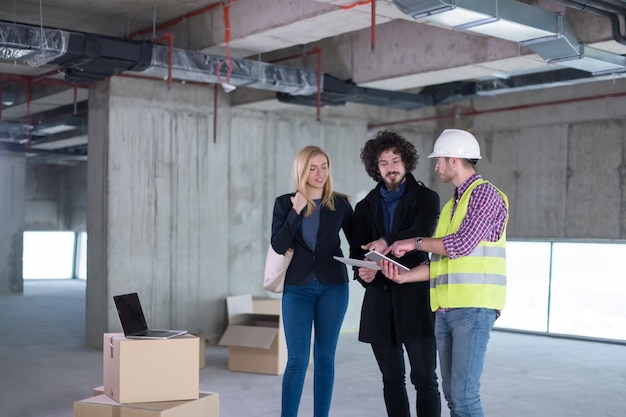 architetto che utilizza un computer tablet mentre mostra i piani di progettazione della casa a una giovane coppia in cantiere