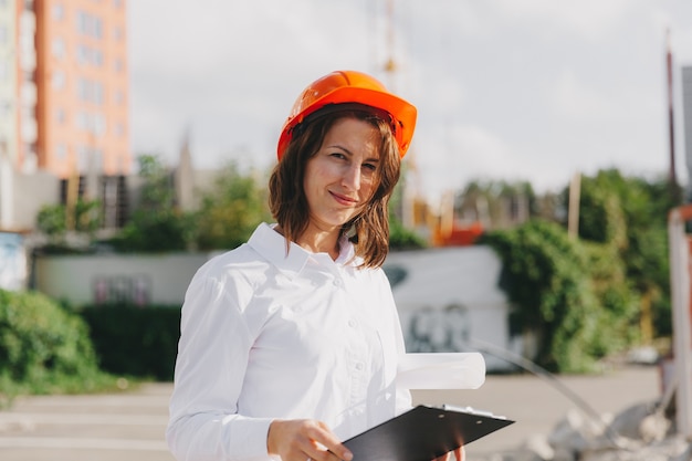 Architetto di giovane bella donna in camicia bianca e elmetto in possesso di un flip board. donna in elmetto in un cantiere edile a casa.