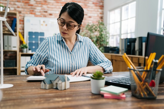 architetto donna asiatica che lavora con laptop e progetti. progetto architettonico dell'edificio di marketing verde con calcolatrice nel design dell'ufficio loft. signora freelance ingegneria conteggio progetto di costruzione