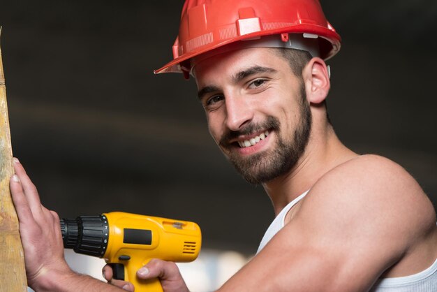 Architetto maschio di successo in un cantiere che cerca di perforare una grande tavola di legno