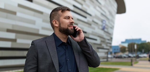 Architetto maschio pensieroso parla al telefono sullo sfondo dell'edificio