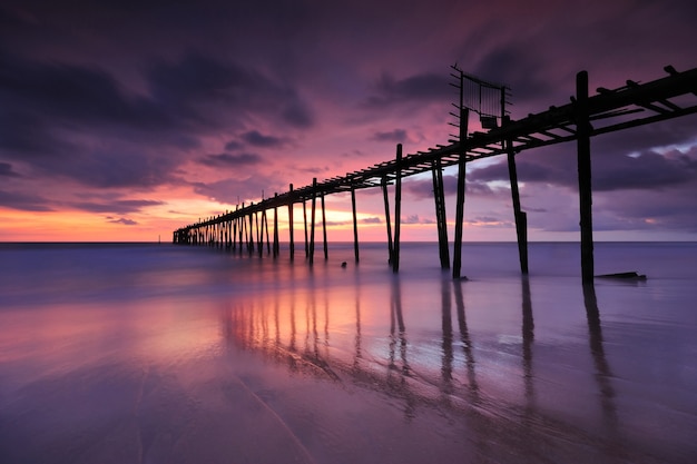 Archivato ponte di legno in mare dopo il tramonto sulla spiaggia