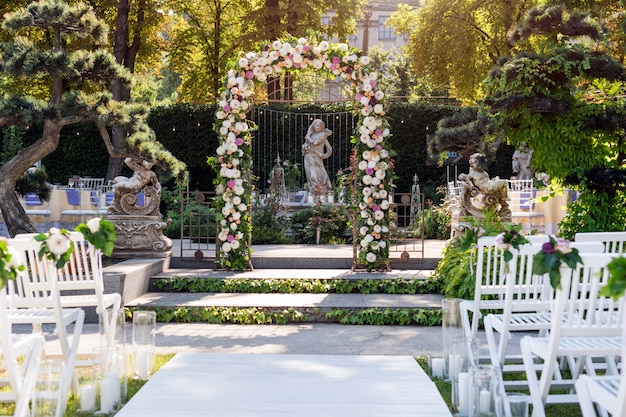 Arco di cerimonia nuziale con i fiori all'aperto. Cerimonia nuziale nel giardino con sculture e fontana.