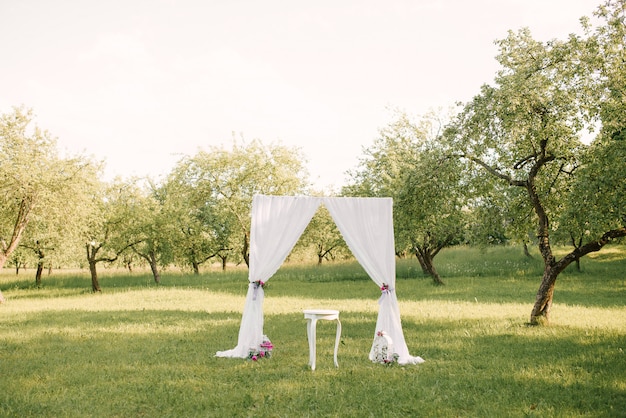 Arco di cerimonia nuziale decorato con il panno e fiori all'aperto. Bel matrimonio allestito. Cerimonia di nozze su prato inglese verde nel giardino.