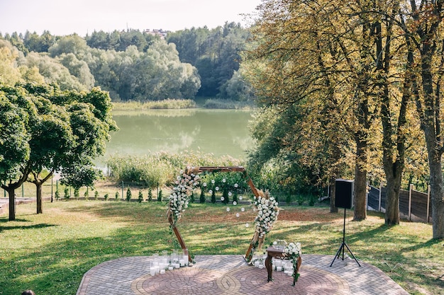 Arco in legno per cerimonia nuziale con bellissimi fiori e lampade retrò sul lago d'autunno