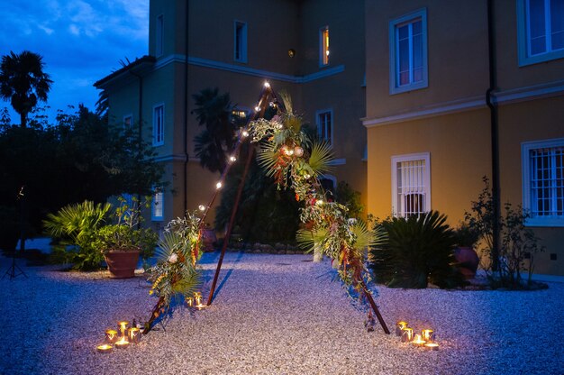 Arco per la cerimonia nuziale la sera a forma di capanna triangolare decorata con fiori e lampadine