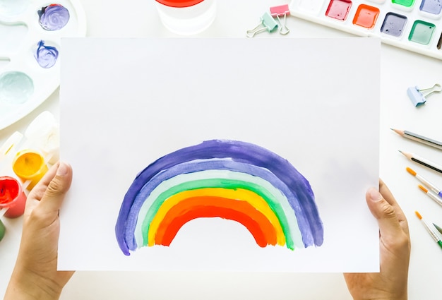 Arcobaleno della pittura della ragazza su carta durante la quarantena di Covid-19 a casa.