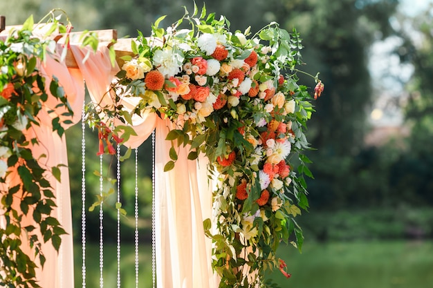 Area della cerimonia di nozze vicino al fiume sul molo. Arco rettangolare in legno, sedie bianche decorate con fiori, verde, petali, foglie e tulle color pesca. Decorazioni rustiche carine e di tendenza