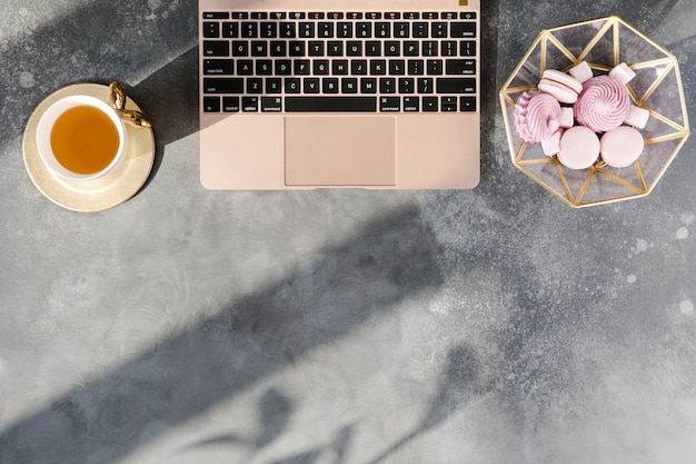 Area di lavoro con il taccuino, il tè e le decorazioni di rosa pastello su fondo grigio.