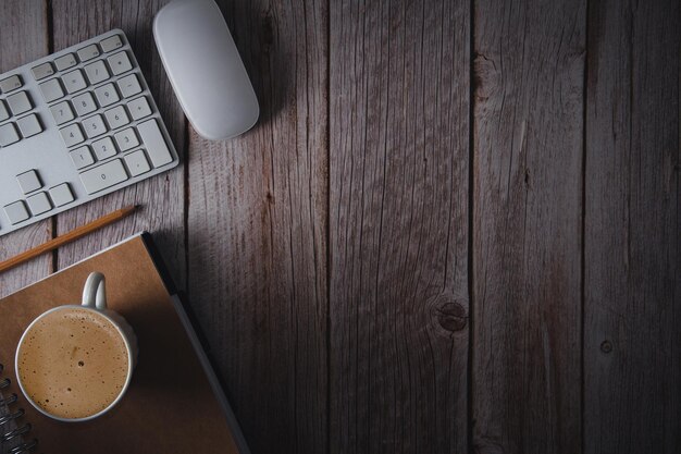 Area di lavoro con la penna del taccuino della tastiera del computer e la tazza di caffè su fondo di legno Vista dall'alto